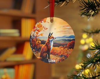 Peut inclure: Ornement de Noël rond représentant un renard dans un paysage d'automne aux teintes orange, jaune et bleu. L'ornement est suspendu à un ruban rouge et le nom "Lisa" est imprimé en bas.