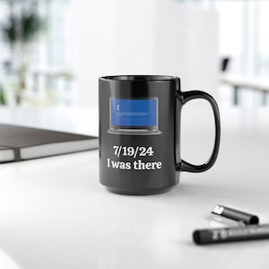 May include: Black coffee mug featuring a white image of a laptop screen displaying the blue screen of death. The text "7/19/24 I was there" is printed below the image.