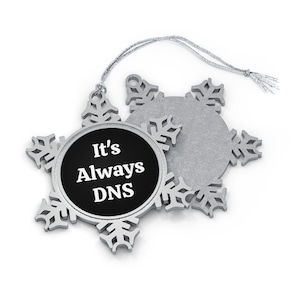 May include: A silver snowflake ornament with a black circle in the center that says "It's Always DNS".