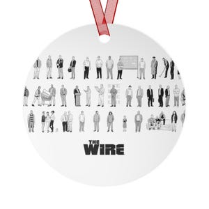 May include: A white, round ornament with a red ribbon for hanging. The ornament features a black and white illustration of various figures, with the text "THE WIRE" at the bottom.