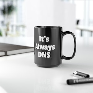 May include: A black ceramic mug with a white inscription that reads "It's Always DNS".