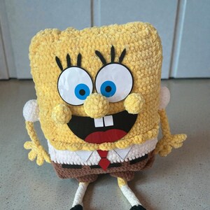 May include: A handmade, plush SpongeBob SquarePants character. The yellow, square-shaped body has large, blue-eyed eyes, a wide black mouth, and a red tie. The arms and legs are detailed, and the plush is made of a soft, textured material.