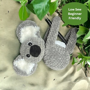 May include: A gray crocheted koala plush toy with black eyes and a black nose. The koala is lying on its back with its arms and legs outstretched. The text "Low Sew Beginner Friendly" is written in a green speech bubble.