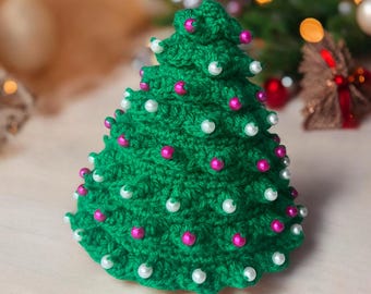 Op de afbeelding: Een groene gehaakte kerstboomversiering versierd met witte en roze kralen.