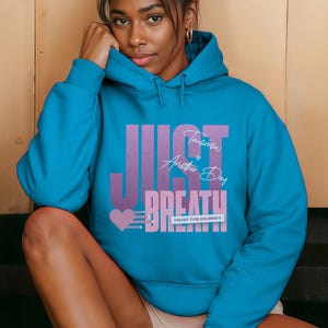 May include: A turquoise hoodie with the words "JUST BREATHE" in a purple and pink design. The text "Tomorrow is Another Day" and "TRUST THE JOURNEY" are also featured on the front of the sweatshirt.