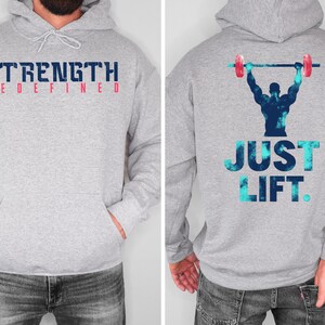 May include: Gray hooded sweatshirt with the text "STRENGTH REDEFINED" on the front and a blue and white graphic of a person lifting weights with the text "JUST LIFT." on the back.