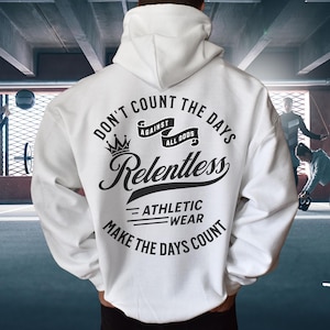 May include: White athletic hoodie with the text "DON'T COUNT THE DAYS AGAINST ALL ODDS Relentless ATHLETIC WEAR MAKE THE DAYS COUNT" in black. The hoodie has a drawstring hood and is being worn in a gym setting.