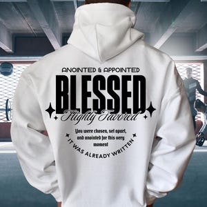 Può includere: Felpa con cappuccio bianca con le parole "ANOINTED & APPOINTED BLESSED Highly Favored" stampate in nero. La felpa ha anche il testo "You were chosen, set apart, and anointed for this very moment IT WAS ALREADY WRITTEN".
