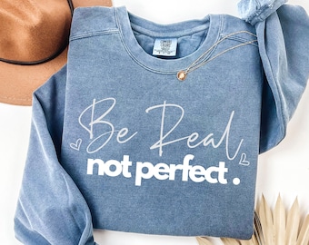 May include: A blue sweatshirt with the text "Be Real not perfect." in white lettering. The sweatshirt has a distressed look and is made of a soft, comfortable fabric.