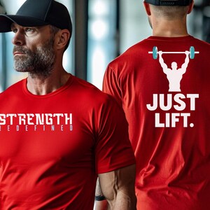May include: Two red t-shirts with white text. One shirt says "STRENGTH REDEFINED" and the other says "JUST LIFT." with a graphic of a person lifting a barbell.
