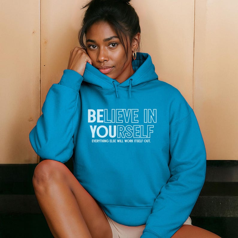 May include: A turquoise hoodie with the text "BELIEVE IN YOURSELF" in white, with the phrase "EVERYTHING ELSE WILL WORK ITSELF OUT" below. The hoodie is worn by a person.