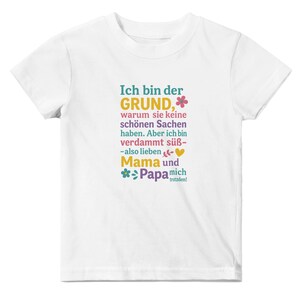 May include: White t-shirt with colorful text in German. The text reads "Ich bin der GRUND" (I am the REASON), followed by more text and the words "Mama" and "Papa". A fun, playful design.