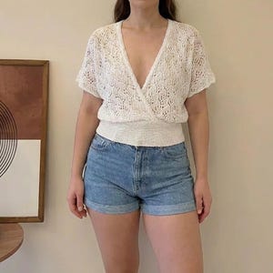 Op de afbeelding: Een witte wikkel top met korte mouwen, een diepe V-hals en een textuur gebreid ontwerp. De top wordt gecombineerd met een spijkerbroek short. De outfit is geschikt voor vrijetijdskleding.