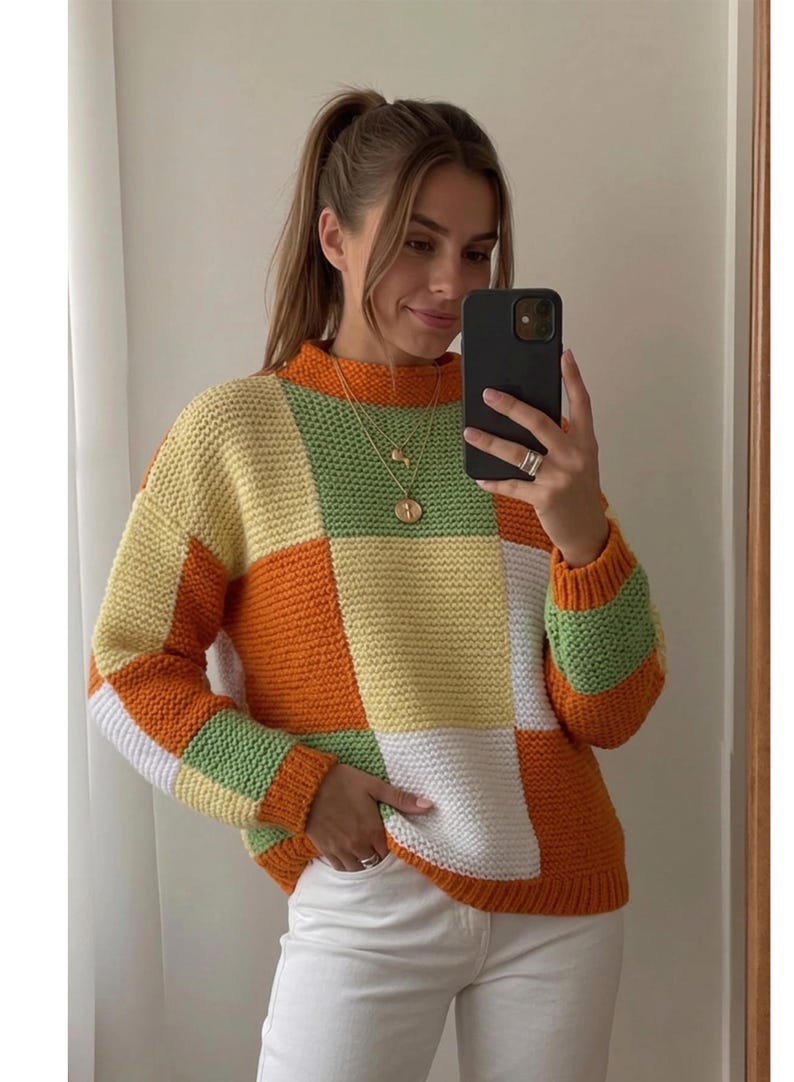 May include: A long-sleeve sweater featuring a color-blocked patchwork design in shades of orange, yellow, white, and light green. The garment has a high neckline and a textured knit pattern throughout, with ribbed cuffs and a ribbed hemline.