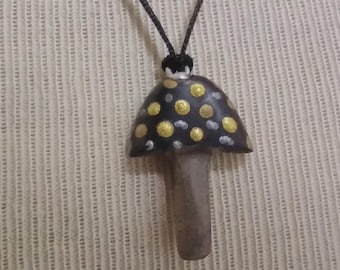 May include: A black and gold mushroom pendant necklace with a black cord. The mushroom has a black cap with gold polka dots and a brown stem.