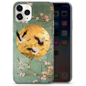 Peut inclure: Une coque de t&eacute;l&eacute;phone transparente avec un motif de trois grues blanches volant devant une lune dor&eacute;e sur un fond floral vert et or.