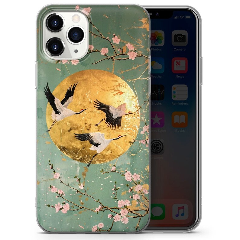 Peut inclure: Une coque de t&eacute;l&eacute;phone transparente avec un motif de trois grues blanches volant devant une lune dor&eacute;e sur un fond floral vert et or.