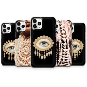 May include: A collection of black phone cases with various designs. Some cases feature a gold-framed eye with blue iris and pearl accents. Other cases showcase a woman's face with pearl jewelry and a skeletal design.