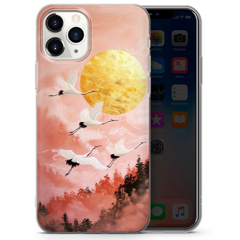 Peut inclure: Une coque de t&eacute;l&eacute;phone transparente avec un motif rose et or repr&eacute;sentant un soleil dor&eacute; et des grues blanches volant dans une for&ecirc;t brumeuse.