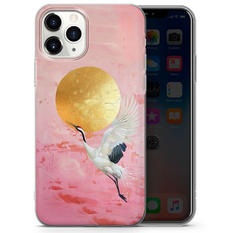Peut inclure: Une coque de t&eacute;l&eacute;phone rose et or avec une grue blanche volant devant un soleil dor&eacute;. La coque est con&ccedil;ue pour un iPhone.