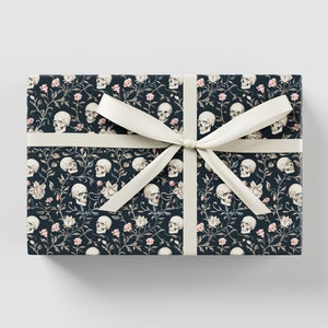 May include: Dark blue gift wrap with a white ribbon. The wrap features a repeating pattern of white skulls and pink flowers.