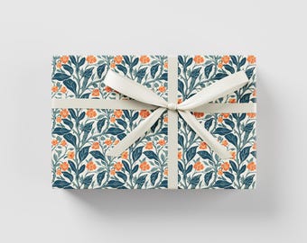 Può includere: Una scatola regalo avvolta in carta bianca con un motivo floreale in tonalità blu e arancio. La scatola è legata con un nastro bianco.
