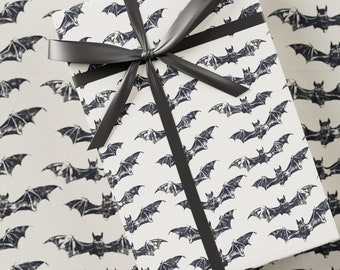 May include: A white gift box with a black bat pattern and a black satin ribbon. The box is wrapped in a Halloween-themed gift wrap.