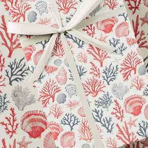 May include: A white gift box with a red and blue coral and seashell pattern. The box is wrapped with a white satin ribbon.