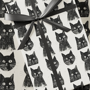 May include: White gift wrap with a black ribbon and a repeating pattern of black cat faces. The cats have large eyes and whiskers.