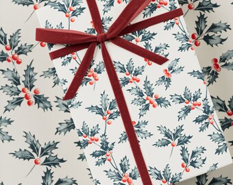 May include: A white gift box with a red ribbon and a holly pattern. The box is wrapped in paper with a repeating pattern of holly leaves and red berries.