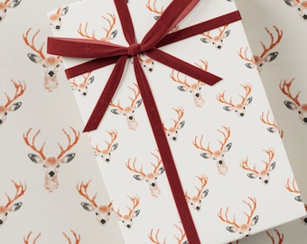 May include: A white gift box with a red velvet ribbon tied in a bow. The box is wrapped in paper with a repeating pattern of brown deer heads with antlers.
