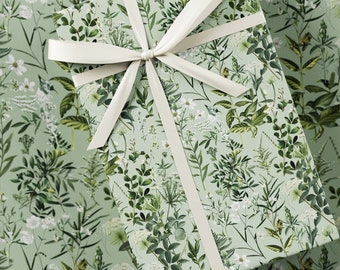 May include: A green gift wrap with a white ribbon tied in a bow. The wrap features a repeating pattern of white flowers and green leaves.