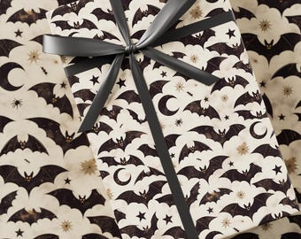 May include: A wrapped gift box featuring a Halloween-themed pattern. The wrapping paper has a cream background with repeating black bats, stars, moons, and spiders. A dark gray ribbon is tied in a bow on top.