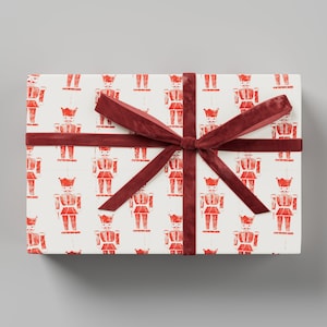 Op de afbeelding: Een witte cadeaudoos met een rood lint en een patroon van rode notenkrakers.