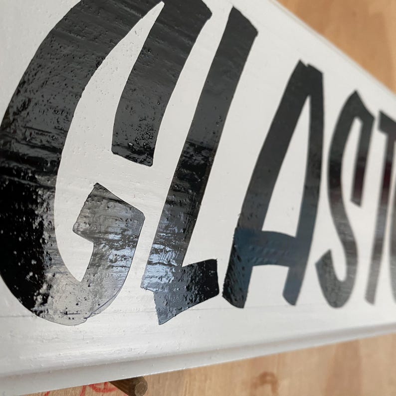 May include: Close-up of a white wooden sign with the word "GLASTONBURY" written in black paint.
