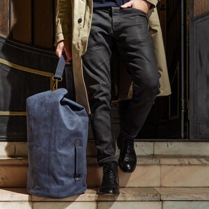 Puede incluir: Una bolsa de viaje azul con cierre enrollable, un asa lateral y una correa de hombro extra&iacute;ble con herrajes de lat&oacute;n. La bolsa est&aacute; hecha de un material mate y texturizado, y presenta una costura vertical en el panel frontal.
