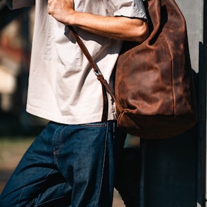 A man holding a leather duffel bag on his shoulder.