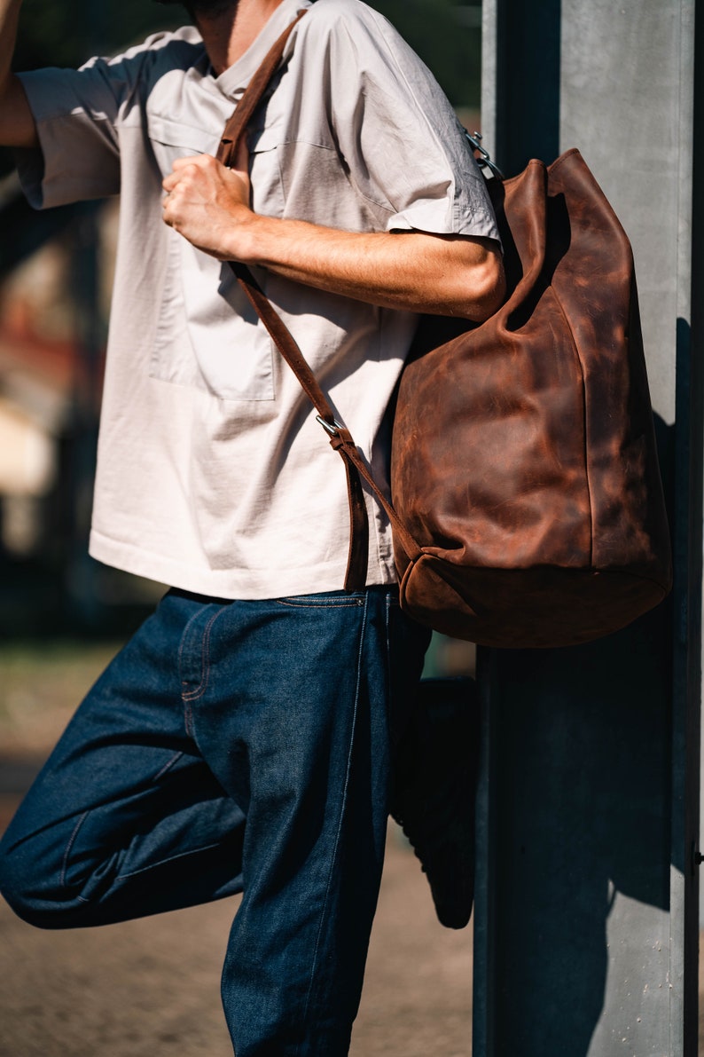 A man holding a leather duffel bag on his shoulder.