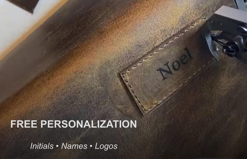 Puede incluir: Una superficie de cuero marr&oacute;n oscuro con un parche rectangular de cuero cosido, con el nombre Noel grabado en negro. El texto FREE PERSONALIZATION Initials &bull; Names &bull; Logos es visible en blanco en la parte inferior de la imagen.