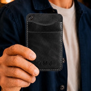 May include: Black leather cardholder with a stitched border and a top eyelet. The cardholder has two card slots and a pocket. The initials "DMJ" are embossed on the front.