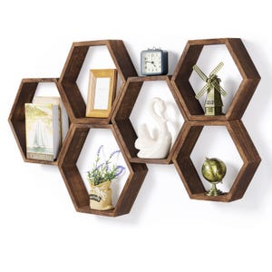 May include: Set of six hexagonal wooden shelves in a honey brown color. The shelves are arranged in a honeycomb pattern on a white wall. The shelves are decorated with various items, including a small clock, a decorative windmill, a white swan figurine, a potted plant, and a small globe.