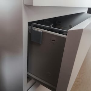 Peut inclure: Un placard blanc avec un tiroir partiellement ouvert. Le tiroir est en bois brun clair et possède une poignée argentée. Le tiroir est vide.