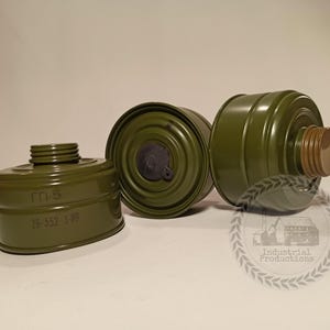 Op de afbeelding: Drie olijfgroene gasmaskerfilters. Eén filter is gemarkeerd met "ГП-5" en "26-552-3-80". De filters hebben een cilindrische vorm met een schroefdraad aan de bovenkant en een bruine dop. De filters zijn op een licht oppervlak geplaatst.