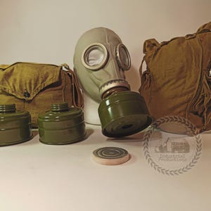 May include: A collection of vintage gas mask equipment. The set includes a grey mask with clear lenses, two green filters, and a khaki bag. There is also a round filter and a larger khaki bag. The items are displayed on a white surface.