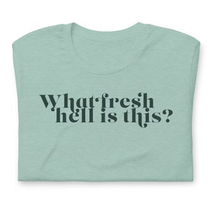 Puede incluir: Una camiseta azul claro con el texto "What fresh hell is this?" impreso en verde oscuro.