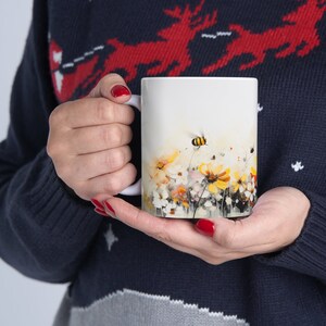 May include: White ceramic mug with a watercolor design of yellow and white flowers and a bee flying over them.