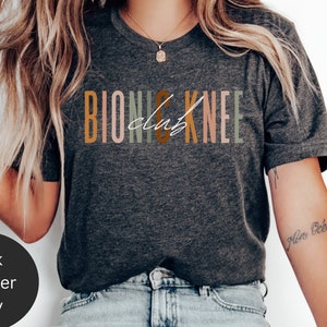 May include: A dark heather grey t-shirt with the text "Bionic Knee Club" printed in colourful letters.