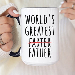 Può includere: Una tazza in ceramica bianca con bordo e manico neri. La tazza ha un testo nero che recita "World's Greatest" con la parola "Farter" cancellata e sostituita da "Father".