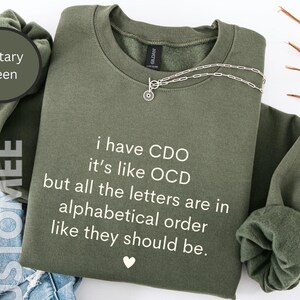 May include: A military green sweatshirt with the text "i have CDO it's like OCD but all the letters are in alphabetical order like they should be." printed in white.