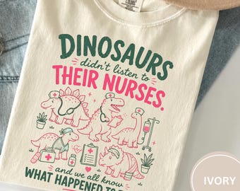 May include: An ivory crew neck t-shirt featuring a graphic print with the text "DINOSAURS didn't listen to THEIR NURSES. and we all know WHAT HAPPENED TO THEM." The design includes illustrations of five dinosaurs wearing nurse caps and medical gear.